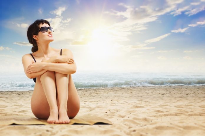 Frau sitzt unter praller Sonne am Strand